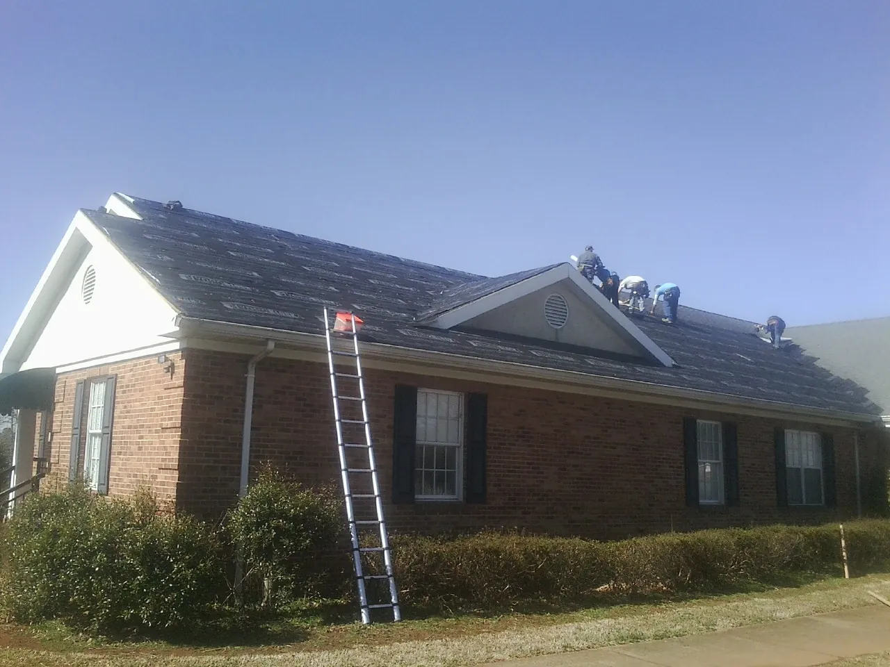 Crew tearing shingles off a brick ranch roof with a ladder set — Emergency Roof Repair work by our crew in La Quinta
