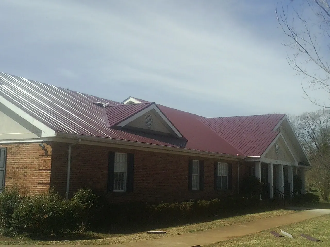 Red metal roof with gabled entries on a long brick building, from a Hail Damage Roof Repair job in La Quinta
