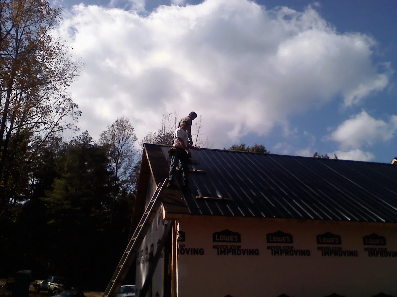 Roofer fastening dark metal panels high against a cloudy sky, from a Roof Inspection job in La Quinta